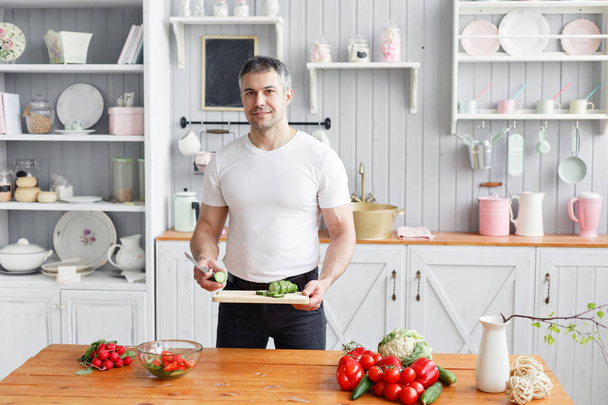 Sportler mittleren Alters, in der Hand eine Schüssel mit einem Teller mit einem vorbereiteten Salat aus Gurken und Tomaten. - Foto, Bild