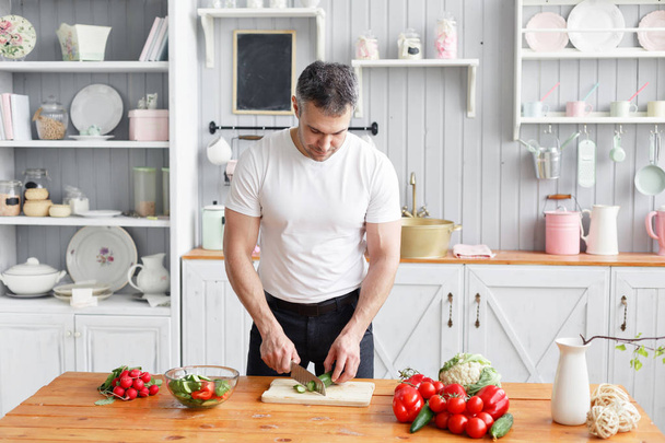 Sportler mittleren Alters, schneidet Gemüsesalat mit Gurken und Tomaten. Vegetarisches Essen - Foto, Bild