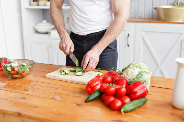 Sportler mittleren Alters, schneidet Gemüsesalat mit Gurken und Tomaten. Vegetarisches Essen - Foto, Bild