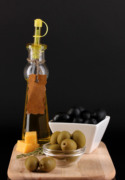 Black and green olives in bowl with rosemary,olive oil and cheese on board isolated on black - Фото, зображення