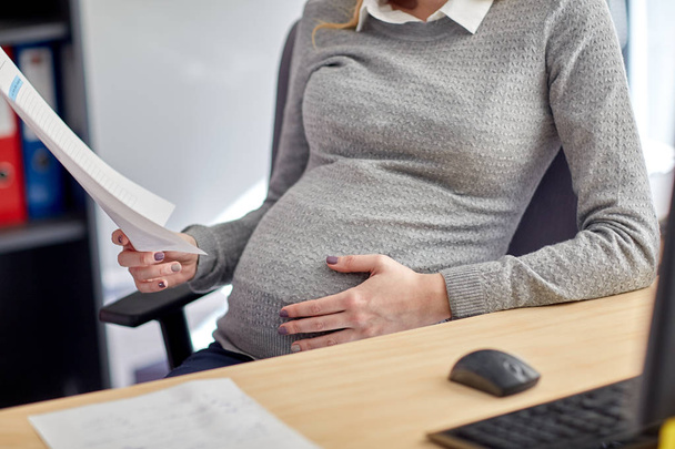 pregnant businesswoman reading papers at office - Foto, afbeelding