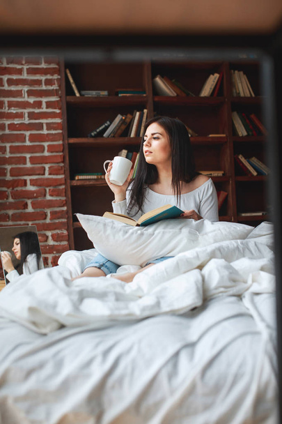 Красивая молодая женщина читает книги и пьет кофе в постели
  - Фото, изображение