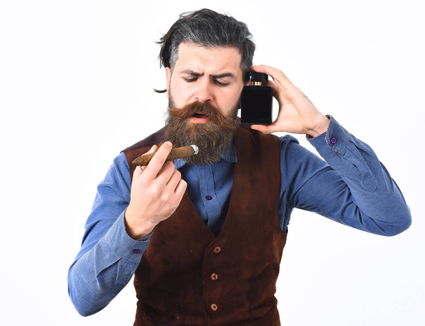 bearded man smoking cigar with serious face, holding perfume - Foto, afbeelding