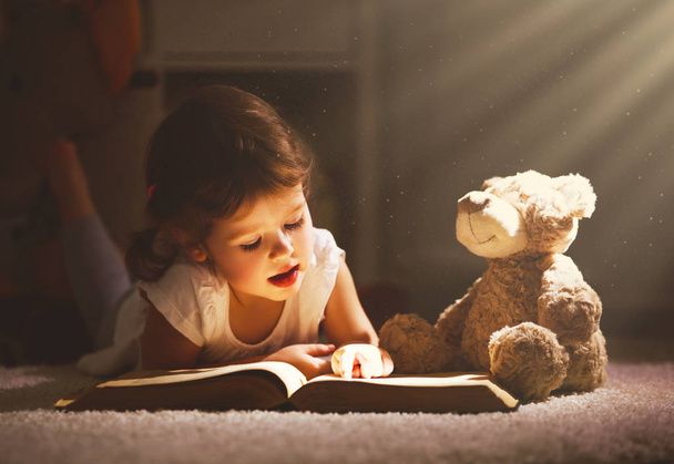 Μικρό παιδί κορίτσι διαβάζοντας ένα βιβλίο το βράδυ στο σκοτάδι με μια να - Φωτογραφία, εικόνα