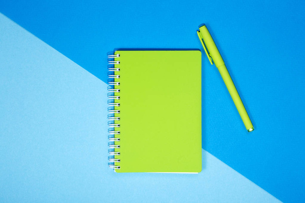 Green notebook and pen on a colored background - Zdjęcie, obraz