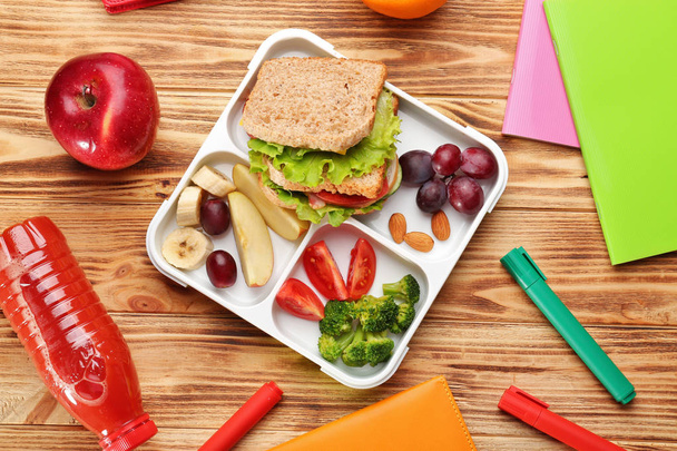 Lunch box with delicious food and stationery on wooden background - Valokuva, kuva