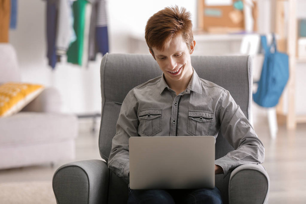 Teenager working with laptop while sitting in arm-chair at home - Photo, image