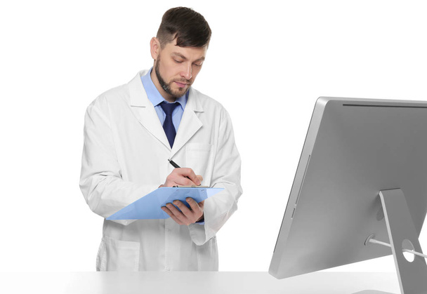 Young pharmacist with clipboard near table on white background - Фото, зображення