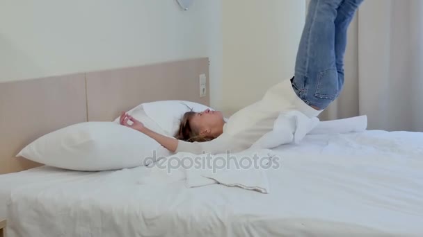 Laughing woman falling into bed and playing with pillows - Záběry, video