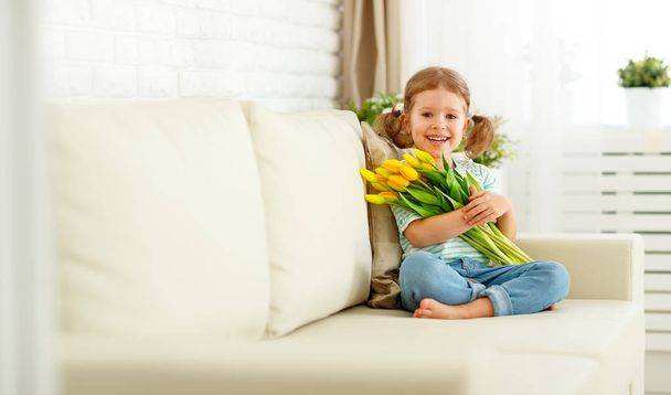 gelukkig lachen kind meisje met gele tulpen thuis - Foto, afbeelding