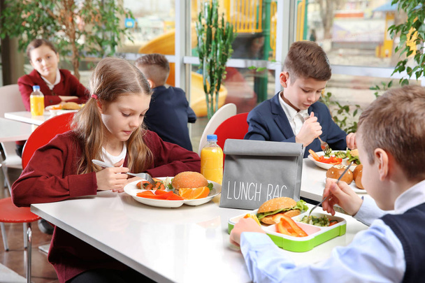 Crianças sentadas na mesa da cafetaria enquanto almoçam - Foto, Imagem