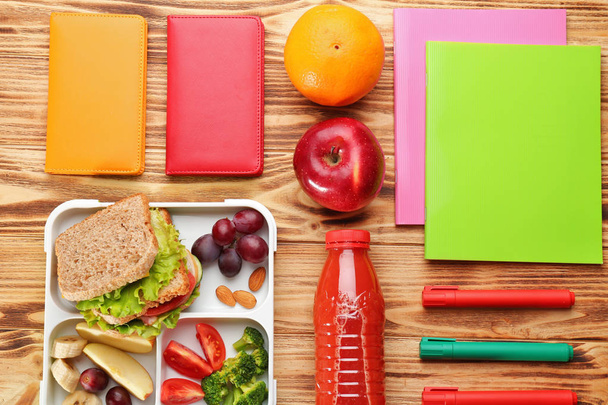 Lunch box with delicious food and stationery on wooden background - Foto, afbeelding