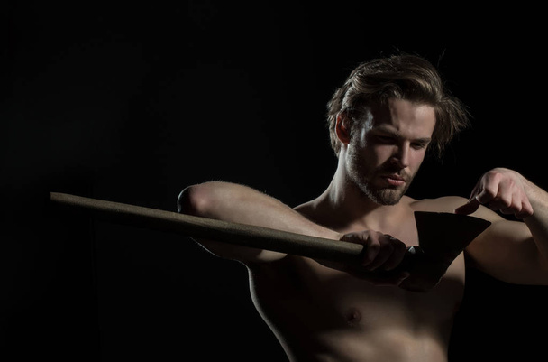 Man touches the ax blade of an ax, a woodcutter or a builder. Naked attractive man on a black background with a tool or cannon. Shirtless muscled fitness lumberjack man with axe - Φωτογραφία, εικόνα