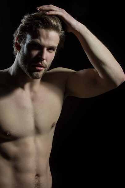 Atraktivní nahý muž dotkne jeho vlasy. Fešák s krásným tělem v ateliéru na černém pozadí - Fotografie, Obrázek