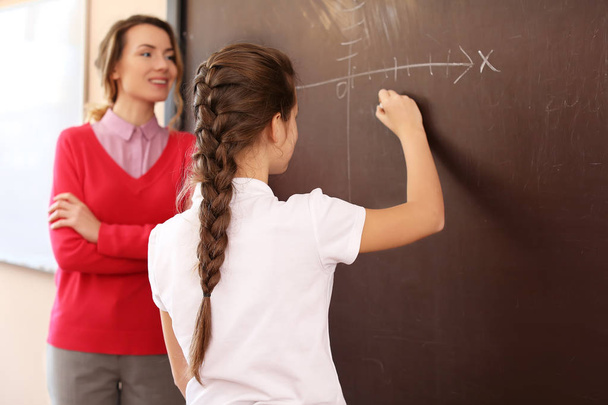Schoolgirl answering at blackboard in classroom - Photo, image