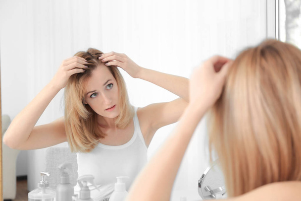 自宅の鏡で見ている脱毛の問題を持つ若い女性 - 写真・画像