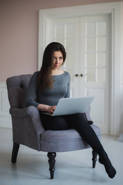 Young woman with laptop sitting on armchair at home - Foto, imagen