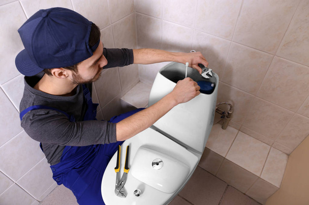 Plumber repairing toilet cistern at water closet - Photo, image