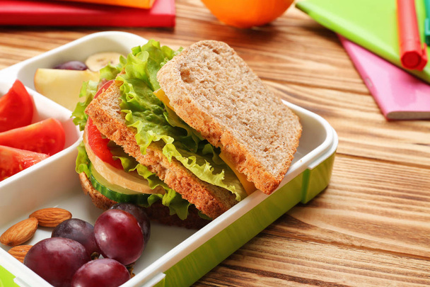 Lunch box with delicious food and stationery on wooden background - Foto, imagen