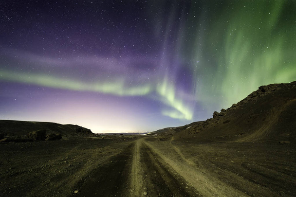 Northern lights blazing over a desert gravel road leading into the distance - Foto, Imagem