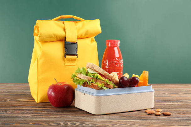 Lunch box with appetizing food and bag on wooden table against chalkboard background - Foto, afbeelding