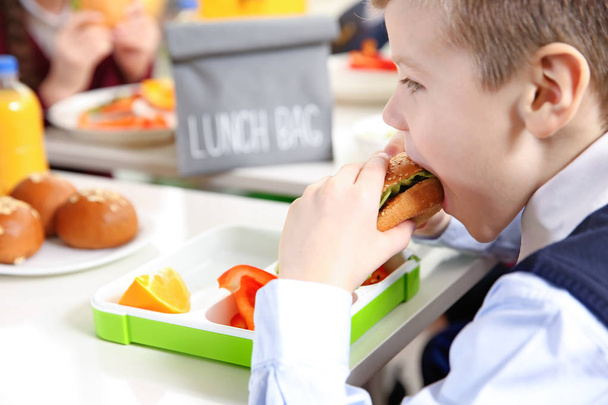 School boy eating sandwich while sitting at table in school cafeteria - Φωτογραφία, εικόνα