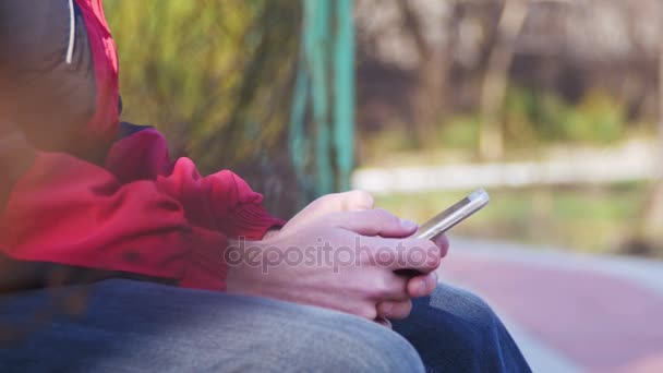 Young Man using a Mobile Phone on a Bench in the City Park - Πλάνα, βίντεο