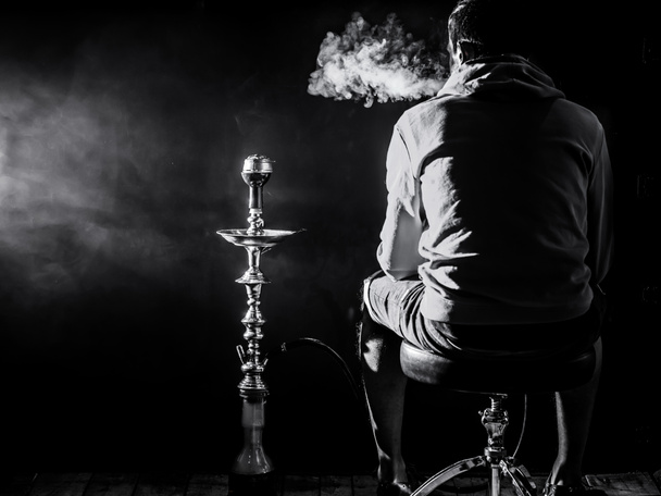 ένας άνθρωπος καπνίζει ναργιλέ σε μαύρο φόντο, όμορφη φωτισμού - Φωτογραφία, εικόνα