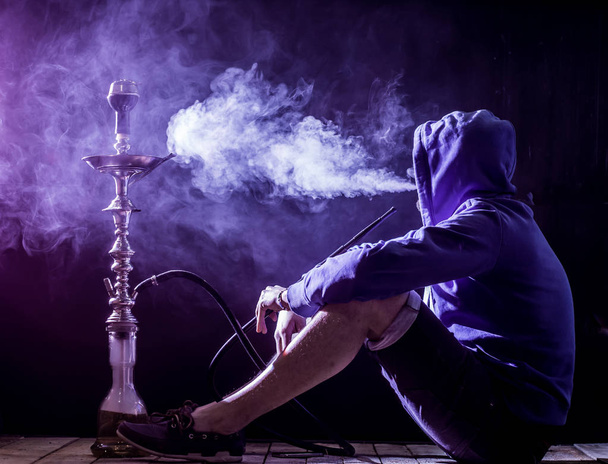 a man smokes a hookah on a black background, beautiful lighting - Фото, зображення