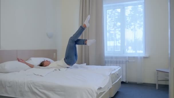 Young blonde woman jumping into white hotel bed - Felvétel, videó