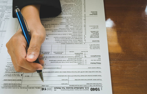 Mujer de negocios mano mantenga la pluma rellene los detalles en el formulario de impuestos
 - Foto, imagen
