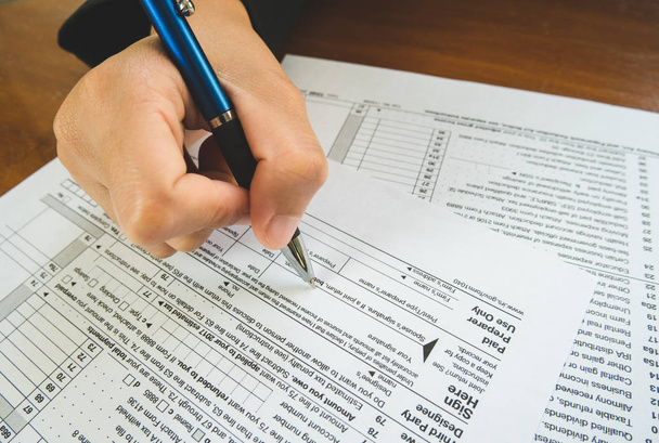 Ручная ручка на знаке на бумаге налоговых форм в бизнесе c
 - Фото, изображение