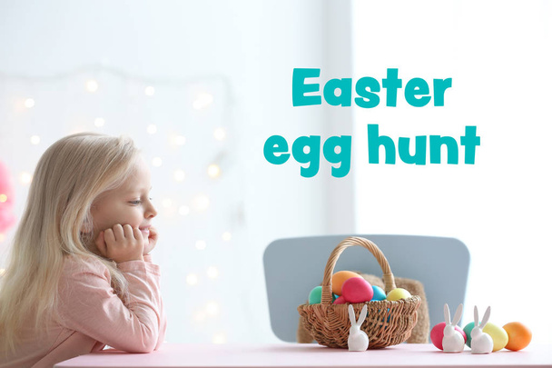 Cute little girl with colorful eggs at home. Text EASTER EGG HUNT on background - Photo, image