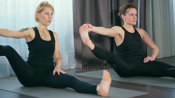 Young women perform asanu padagushthasana from the sitting position - Filmati, video