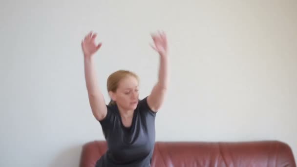 A housewife woman does fitness exercises for the first time, looking at the tablet and TV, it is difficult and unfamiliar, she is tired. - Video