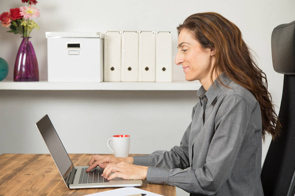 πλευρά γυναίκα που χρησιμοποιούν φορητό υπολογιστή στο γραφείο - Φωτογραφία, εικόνα