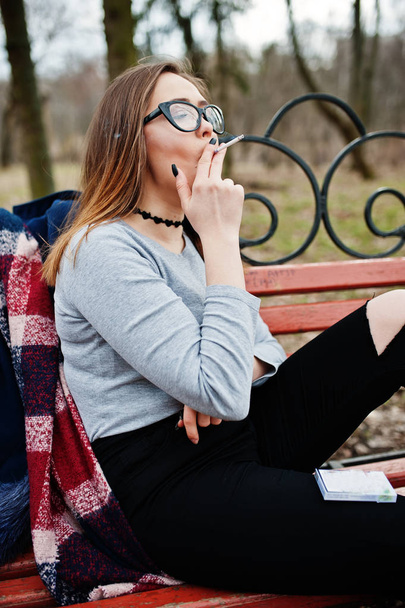 Young girl smoking cigarette outdoors sitting on bench. Concept  - Fotoğraf, Görsel