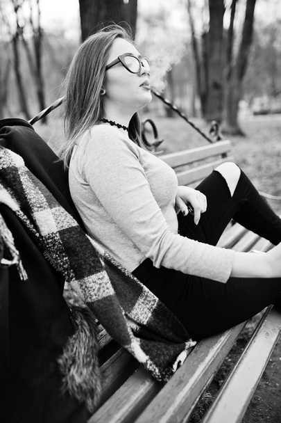 Young girl smoking cigarette outdoors sitting on bench. Concept  - 写真・画像