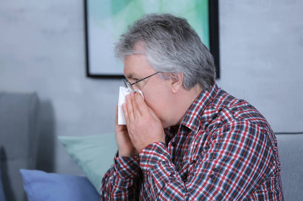 Senior man blowing nose on tissue at home - Фото, изображение