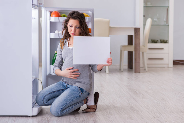 Zwangere vrouw in de buurt koelkast met een leeg bericht - Foto, afbeelding
