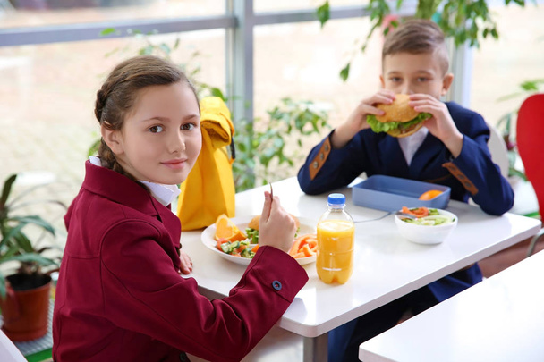 Children sitting at cafeteria table while eating lunch - Photo, image