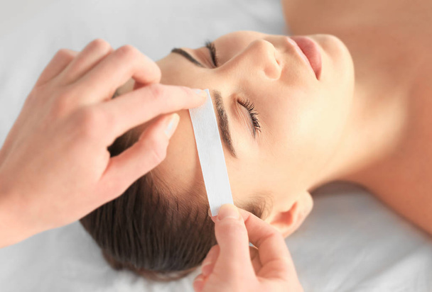 Beautician waxing young woman's eyebrows in spa center - Zdjęcie, obraz