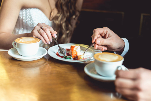 the bride and groom drinking coffee and eating cake in a cafe at the wooden table - Foto, Bild