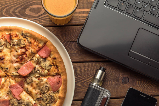 Pizza mit Schinken und Pilzen auf einem Teller, Laptop, elektronischer Zigarette oder Vape - Foto, Bild