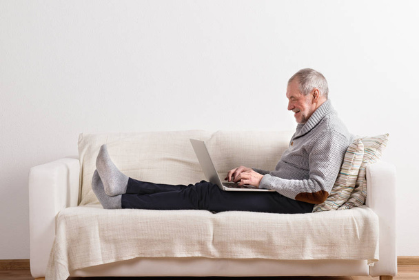 Senior man sitting on sofa, working on laptop. - Foto, afbeelding