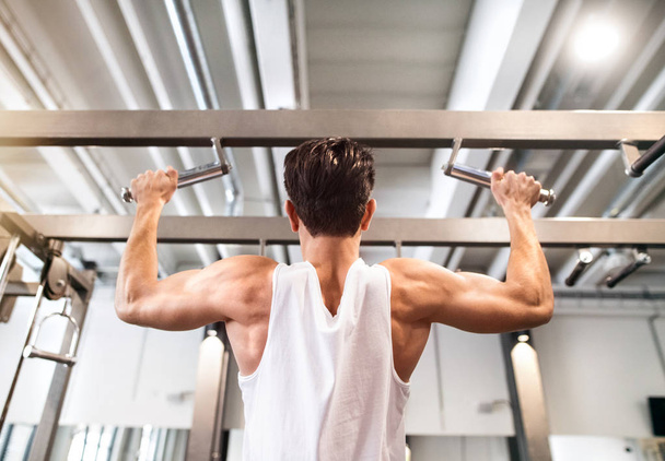 Hispanic man in gym doing pull-ups on horizontal bar. - Foto, Imagen