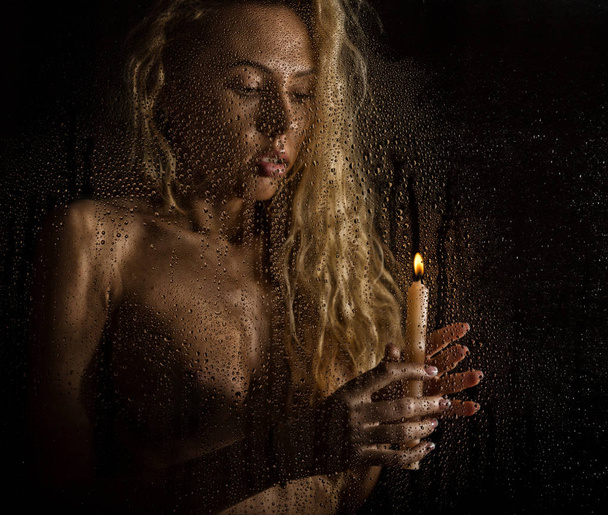 curly nude blonde woman with candle on dark background - Fotografie, Obrázek