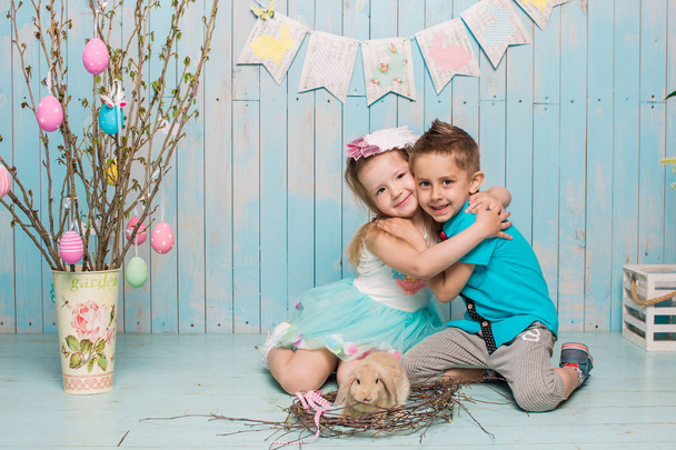 Two little childs, boy, girl, brother and sister along with rabbit sitting on the floor in bright blue clothes Easter, eggs, festive mood, emotion and smile surprise holiday celebration - Foto, immagini