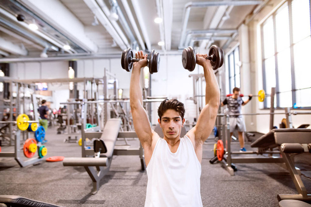 Hispanic man in gym sitting on bench, working out with weights - Fotó, kép