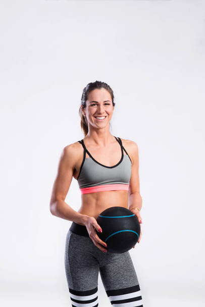 Fit woman in sports clothing holding medicine ball, studio shot - Foto, afbeelding